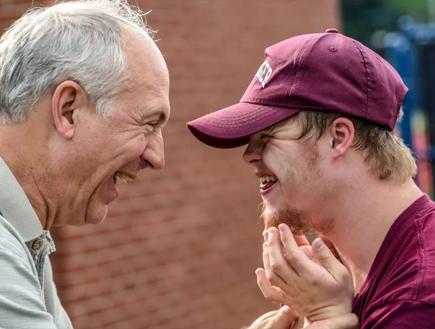 Two men laughing together while one of them is wearing a hat.