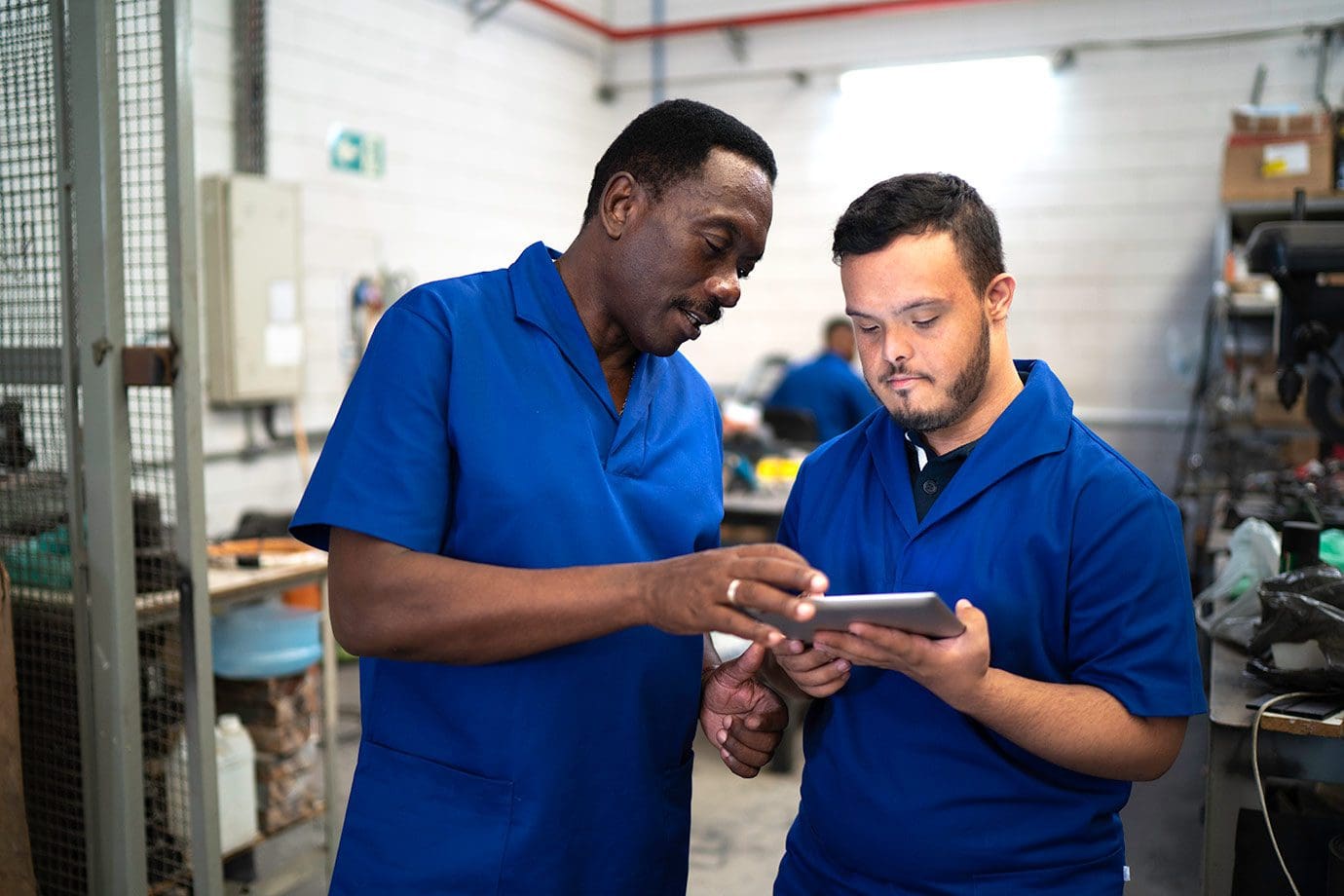 Two men in blue shirts looking at a tablet.