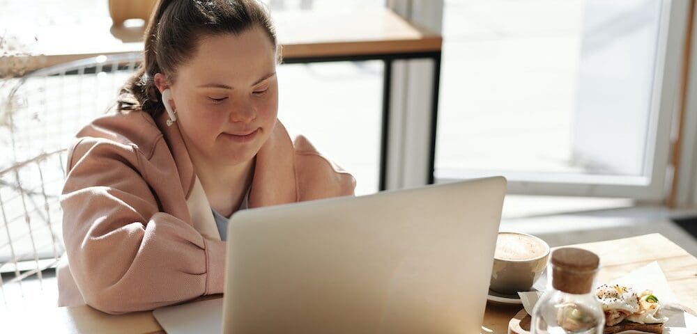 A woman sitting at a table looking at her laptop.